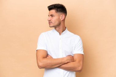 Beyazlı genç adam bej arka planda izole edilmiş, kollarını çapraz tutuyor.