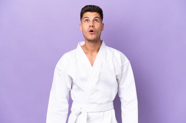 Mor arka planda karate yapan genç beyaz adam şaşırmış bir ifadeyle yukarı bakıyor.