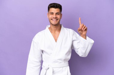 Mor arka planda karate yapan genç beyaz adam en iyinin işareti olarak parmağını kaldırıyor.