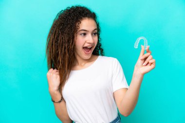 Mavi arka planda izole edilmiş görünmez diş telleri tutan genç bir Arap kadın zaferi kutluyor.