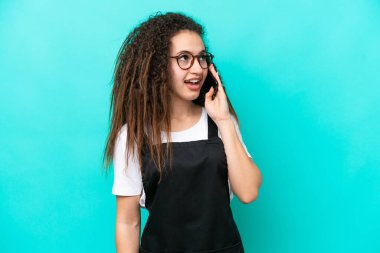 Restoran garsonu Arap kadın mavi arka planda izole edilmiş cep telefonuyla sohbet ediyor.