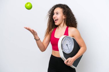 Beyaz arka planda, tartı makinesi ve elmayla izole edilmiş genç bir Arap kadın.