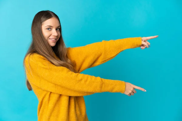若いリトアニアの女性は 側に指を指して 製品を提示青い背景に隔離 — ストック写真