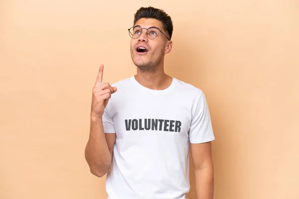 Young Volunteer Caucasian Man Isolated Beige Background Pointing Surprised — Stock Photo, Image