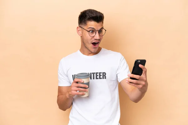 Jonge Vrijwilliger Kaukasische Man Geïsoleerd Beige Achtergrond Houden Koffie Mee — Stockfoto