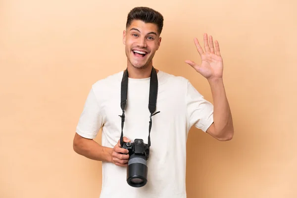 Jonge Fotograaf Kaukasische Man Geïsoleerd Beige Achtergrond Salueren Met Hand — Stockfoto