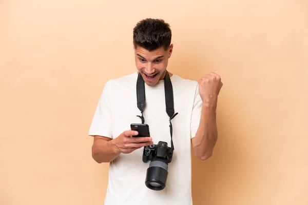 若い写真家Caucasian男孤立上ベージュ背景驚きとメッセージを送信 — ストック写真