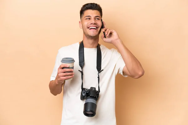 若い写真家Caucasian男隔離オンベージュ背景保持コーヒーへ取り去るとAモバイル — ストック写真