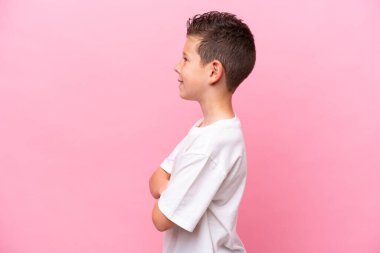 Küçük beyaz çocuk, pembe arka planda, yanal pozisyonda izole edilmiş.