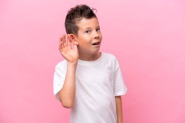 Küçük beyaz çocuk pembe arka planda izole edilmiş bir şekilde bir şeyler dinliyordu. Elini kulağına koyarak.