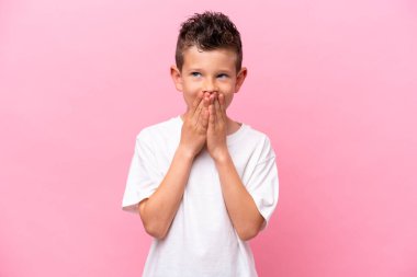 Küçük beyaz çocuk pembe arka planda izole edilmiş mutlu ve gülümseyen elleriyle ağzını kapatıyor.