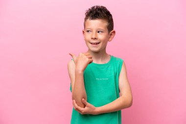 Pembe arka planda izole edilmiş küçük beyaz çocuk bir ürünü sunmak için kenarı işaret ediyor.