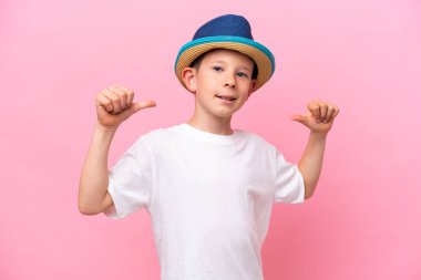 Pembe arka planda izole edilmiş şapka takan küçük beyaz çocuk gururlu ve kendini beğenmiş.