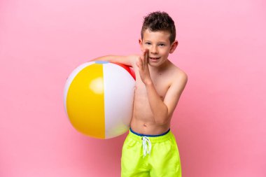 Pembe arka planda izole edilmiş bir plaj topu tutan küçük beyaz çocuk bir şeyler fısıldıyor.