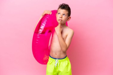 Küçük beyaz bir çocuk pembe arka planda izole edilmiş şişirilebilir bir çörek tutuyor.