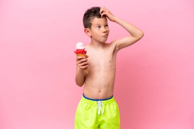 Küçük beyaz bir çocuk pembe arka planda izole edilmiş dondurma yiyor. Şüpheleri var ve kafası karışık.