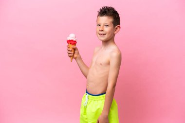 Pembe arka planda izole edilmiş dondurma yiyen beyaz bir çocuk.