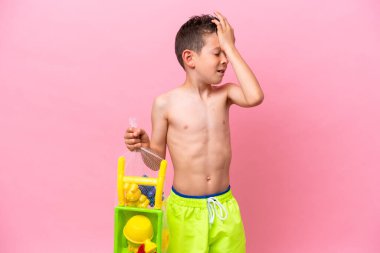 Pembe arka planda izole edilmiş plaj oyuncakları tutan küçük beyaz çocuk bir şey fark etti ve çözüme niyetlendi.