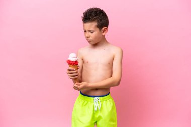 Pembe arka planda, üzgün bir ifadeyle izole edilmiş dondurma yiyen küçük beyaz çocuk.