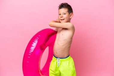 Küçük beyaz bir çocuk pembe arka planda izole edilmiş şişme bir çörek tutuyor.