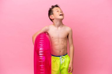 Küçük beyaz çocuk pembe arka planda izole edilmiş şişme bir çörek tutuyor.