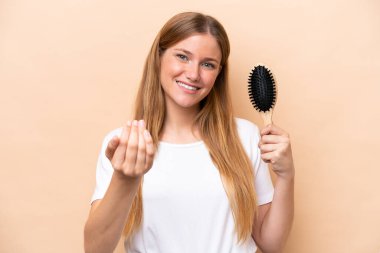 Saçları taranmış, bej arka planda genç, güzel, sarışın bir kadın. Eli ile gelmesi için davet ediyor. Gelmene sevindim.