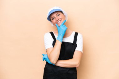 Balıkçı beyaz kadın önlük takıyor ve bej arka planda izole edilmiş çiğ bir balığı tutuyor mutlu ve gülümsüyor.