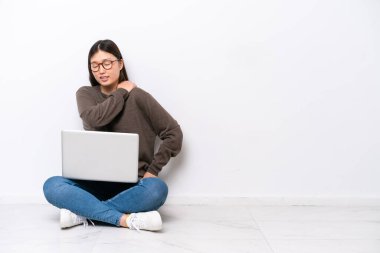 Dizüstü bilgisayarı olan genç bir kadın omuz ağrısından muzdarip olarak yerde oturuyor.