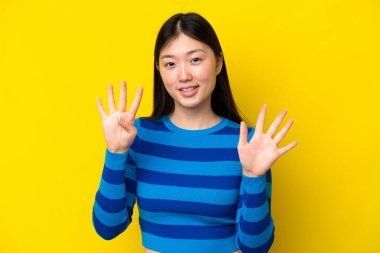 Sarı arka planda izole edilmiş genç Çinli kadın parmaklarıyla dokuz kişi sayıyor.