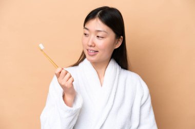 Bej arka planda diş fırçasıyla izole edilmiş genç bir Çinli kadın.