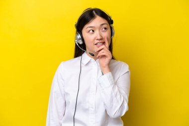 Tele pazarlamacı Çinli bir kadın sarı arka planda izole edilmiş bir kulaklıkla çalışırken bir fikir arıyor.