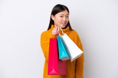 Beyaz arka planda izole edilmiş genç bir Çinli kadın alışveriş torbaları tutuyor ve gülümsüyor.