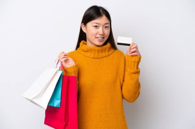 Beyaz arka planda izole edilmiş genç bir Çinli kadın elinde alışveriş çantaları ve bir kredi kartı tutuyor.