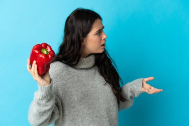 Mavi arka planda karabiber tutan beyaz bir kadın. Şaşırtıcı bir yüz ifadesi var.