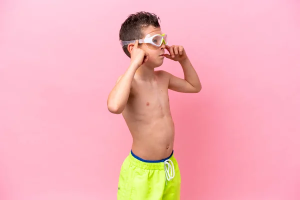 一个戴着粉色背景的潜水护目镜的高加索小男孩有着怀疑和思考 — 图库照片