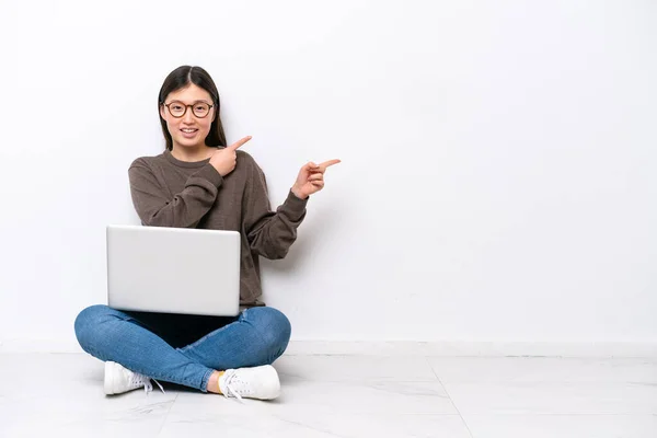 一个年轻的女人 带着笔记本电脑坐在地板上 手指指向旁边 展示着一种产品 — 图库照片