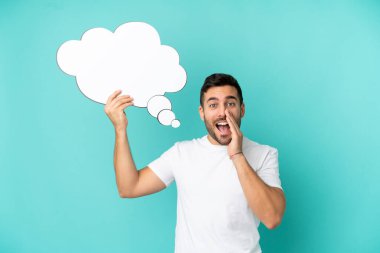 Genç, yakışıklı, beyaz bir adam mavi arka planda izole edilmiş. Elinde düşünce balonu ve bağırış çağırış var.