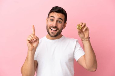 Young man holding a Bitcoin isolated on pink background showing and lifting a finger in sign of the best