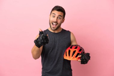 Pembe arka planda izole edilmiş genç bisikletçi. Başparmakları havada. Çünkü iyi bir şey oldu.