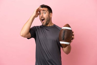 Pembe arka planda ragbi oynayan beyaz bir adam yan tarafa bakarken sürpriz jest yapıyor.