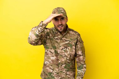 Asker, sarı arka planda izole edilmiş. Bir şeye bakmak için çok uzaklara bakıyor.