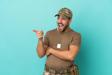 Mavi arka planda izole edilmiş künyeli ordu parmak göstererek bir ürün sunuyor.
