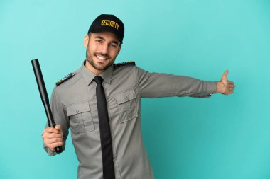 Genç güvenlik görevlisi mavi arka planda izole edilmiş. Davet etmek için ellerini yana uzatıyor.