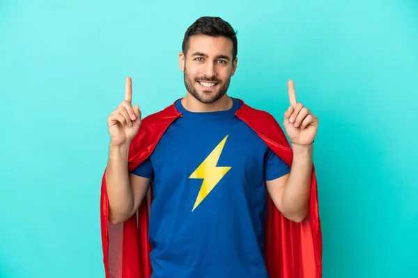 Super Hero caucasian man isolated on blue background pointing up a great idea