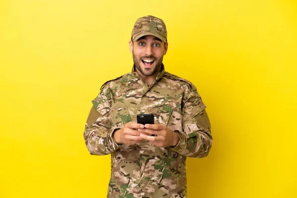 Military man isolated on yellow background surprised and sending a message