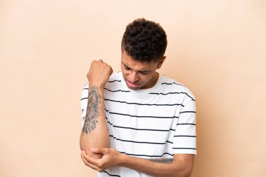Bej arka planda izole edilmiş genç Brezilyalı adam dirseğinde ağrı var.