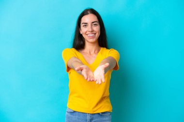 Mavi arka planda izole edilmiş genç beyaz kadın bir ilan vermek için avucunun içinde hayali bir fotokopi makinesi tutuyor.