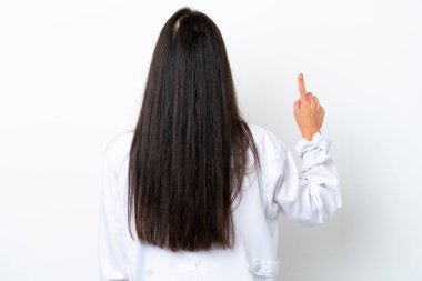 Beyaz arka planda izole edilmiş beyaz bir kadın doktor önlüğü giyiyor ve arkasını işaret ediyor.