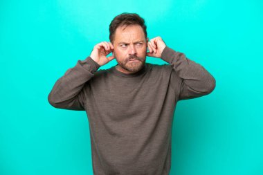 Middle age caucasian man isolated on blue background frustrated and covering ears
