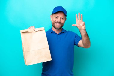 Orta yaşlı bir adam mavi arka planda izole edilmiş yiyecek paketini alıyor mutlu ve parmaklarıyla dört tane sayıyor.